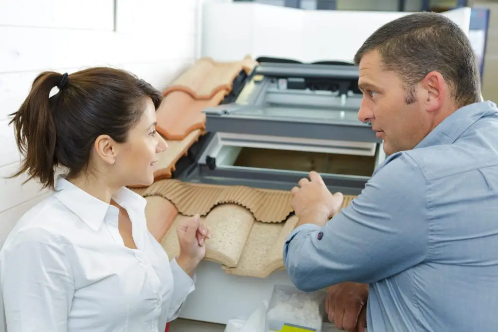 A man and a woman in a showroom examining and pointing at roof tile samples on a display model.