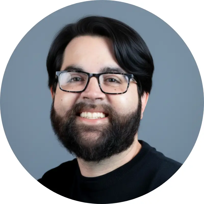Headshot of Adam Surridge, Creative Coordinator at Capital Valley Marketing, a smiling man with a beard and glasses wearing a dark shirt against a light grey background.